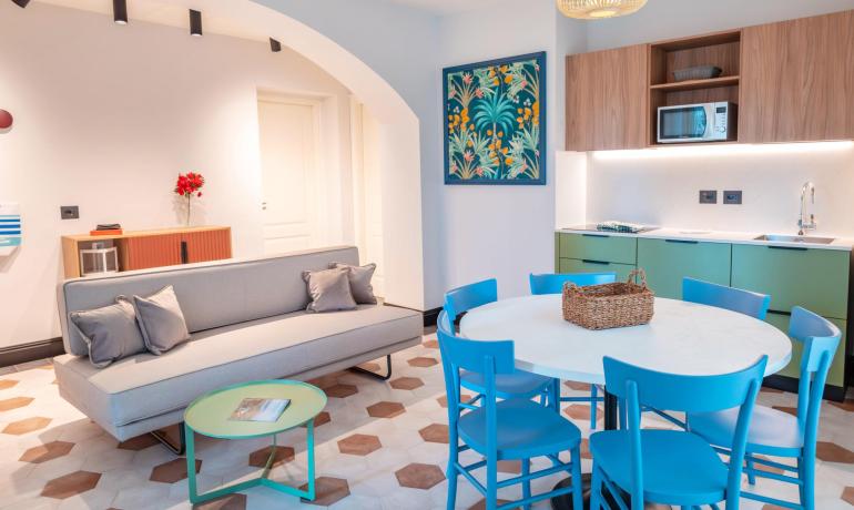 Modern living room with kitchen, gray sofa, and table with blue chairs.