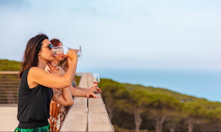 Two women drinking wine with an ocean view.