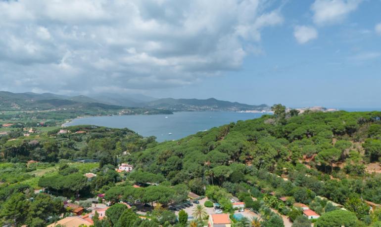 Vista panoramica su mare e colline verdi sotto un cielo nuvoloso.