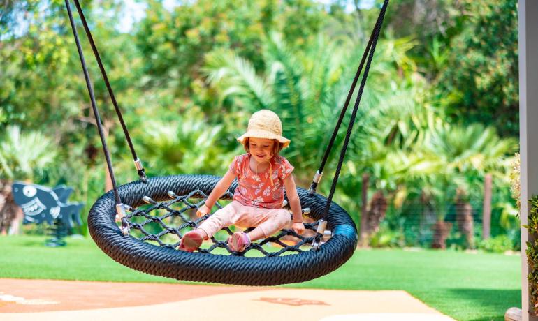 Enfant sur une balançoire nid dans un parc ensoleillé.